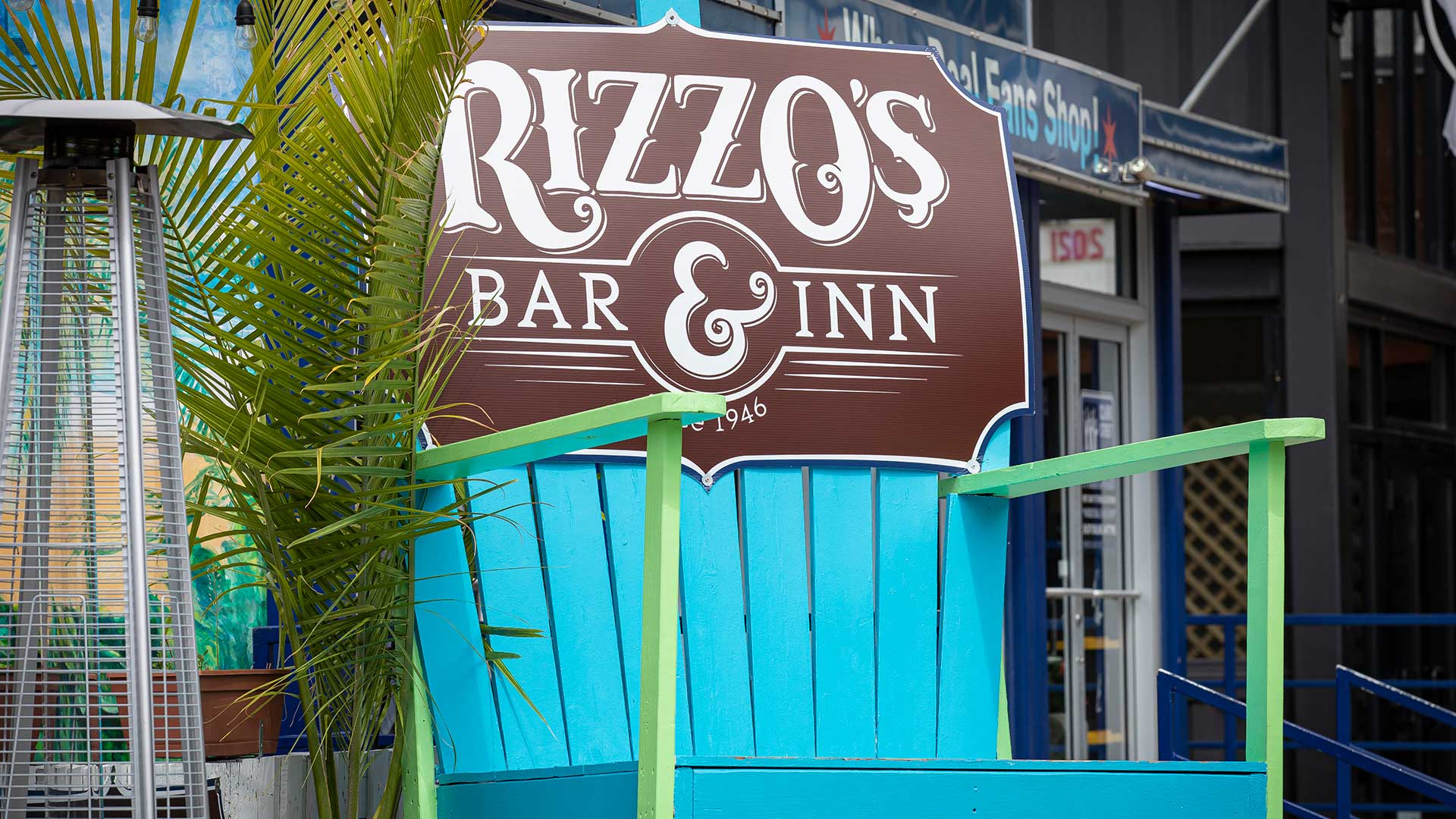 An over-sized chair with a bar sign on it in front of bar.