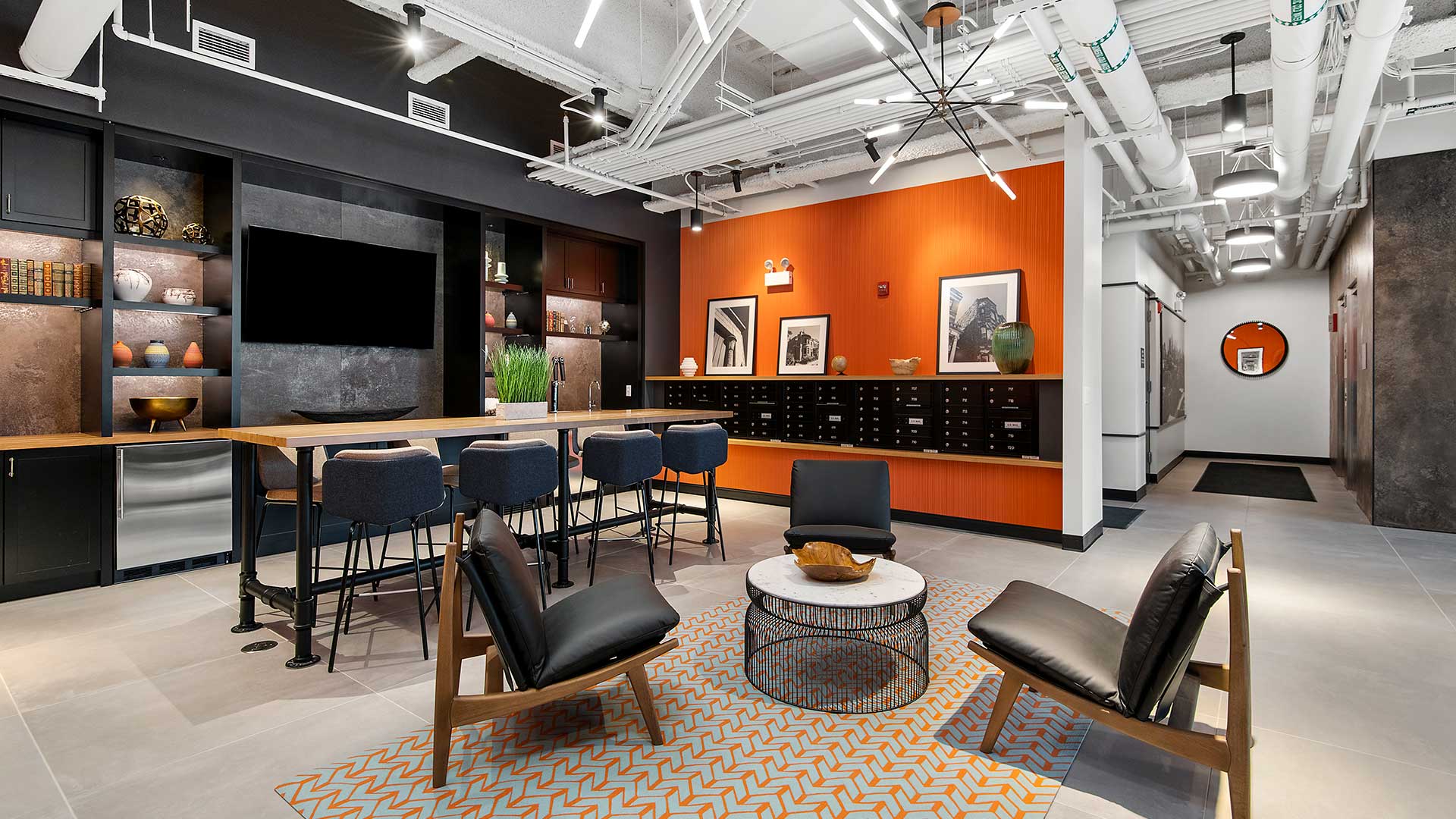 Looking in to the Clubroom room from the lobby at Wrigleyville Lofts. Club chairs are seen ahead with a high-top table off to the left in front of a mounted television. The elevator lobby is seen off to the right.
