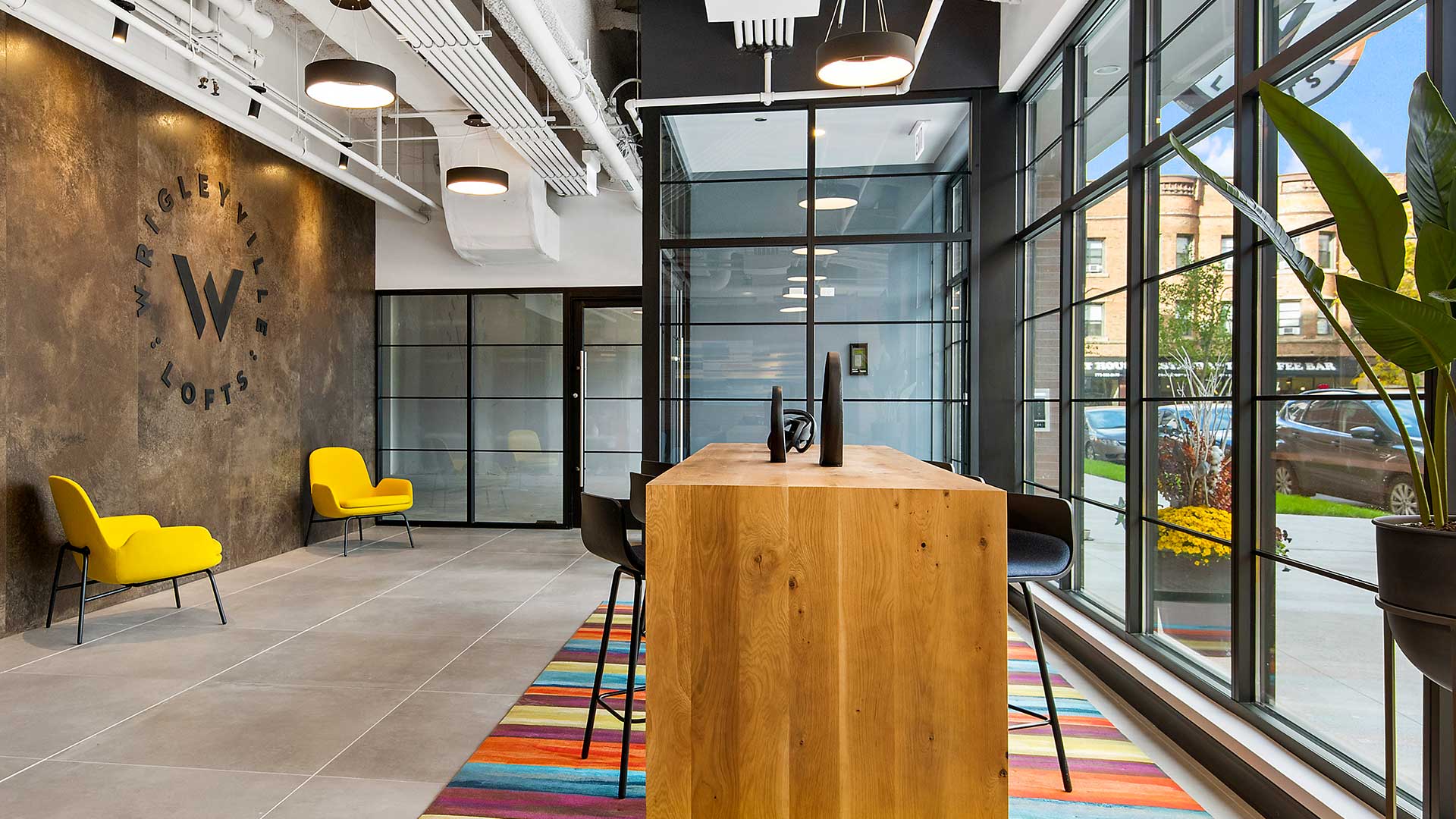 Looking across a high-top table in the lobby at Wrigleyville Lofts. The main entrance is behind with windows to the right and the logo wall to the left.