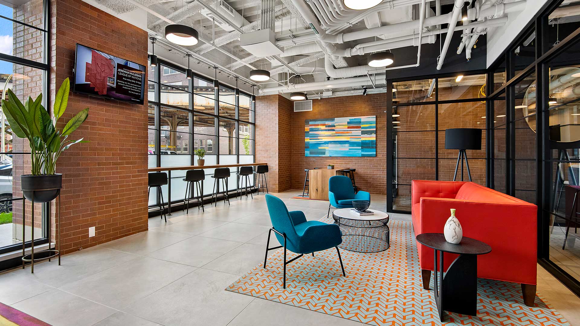 Brightly colored furniture sits along the interior windows in the lobby at Wrigleyville Lofts. The exterior windows are off the left with a stools and a bar lining them.