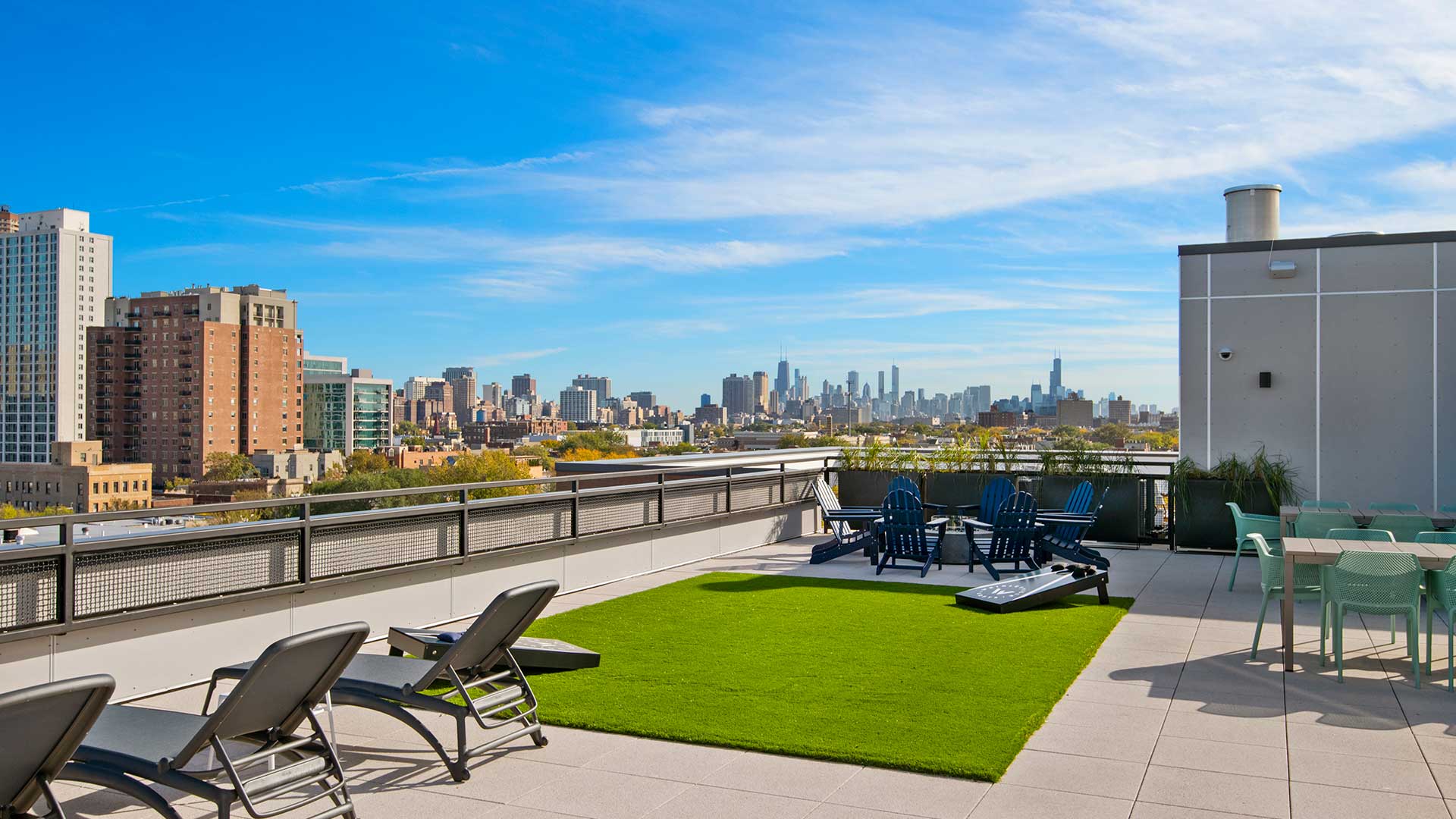 The rooftop deck at Wrigleyville Lofts with the Chicago skyline in the distance. Several lounge chairs line the left with turf and a bags game ahead.
